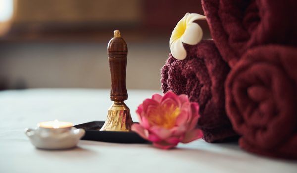 Metal bell for inviting guests to thai procedures surrounded with exotic flowers and candles near towels